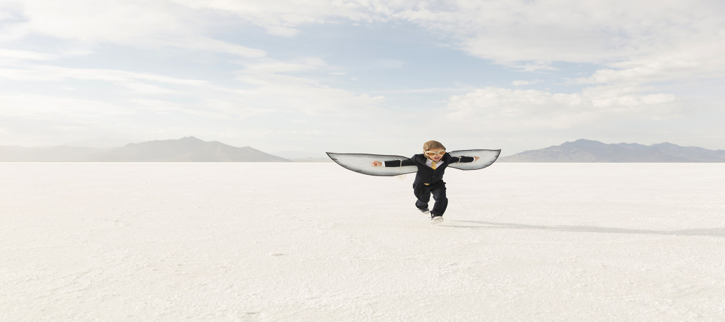A young business boy dressed in business suit and wearing cardboard wings and aviator goggles is ready to fly his business into the sky. He is running on the Bonneville Salt Flats in Utah, USA.